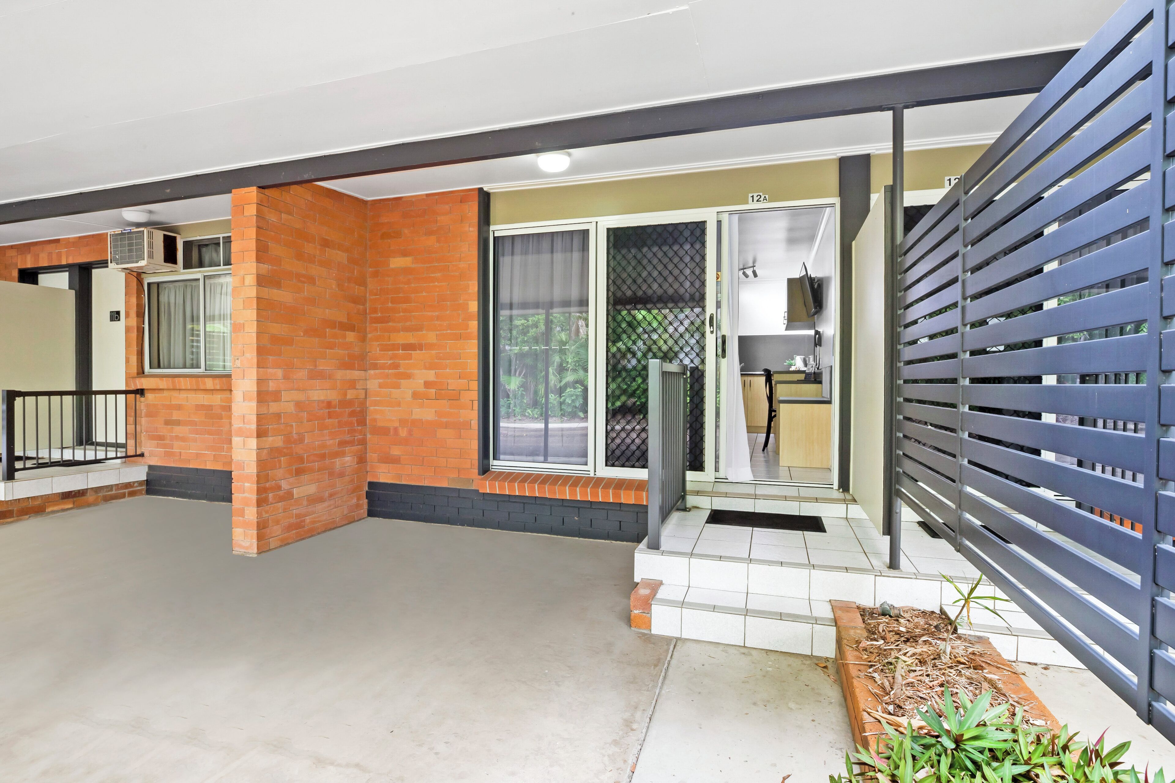 A modern hotel room with a brick wall, a sliding glass door, a small balcony with a wooden planter, and a metal railing.