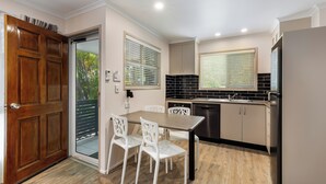Cocina pequeña con una mesa de comedor, sillas blancas y una puerta de madera.
