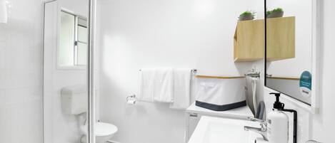 Ein modernes Badezimmer mit Duschkabine aus Glas, weißer Toilette, Waschbecken mit Spiegel und Holzregal mit Pflanzen.