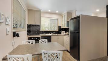 A modern kitchen with a dining table, chairs, a refrigerator, and a window with blinds.