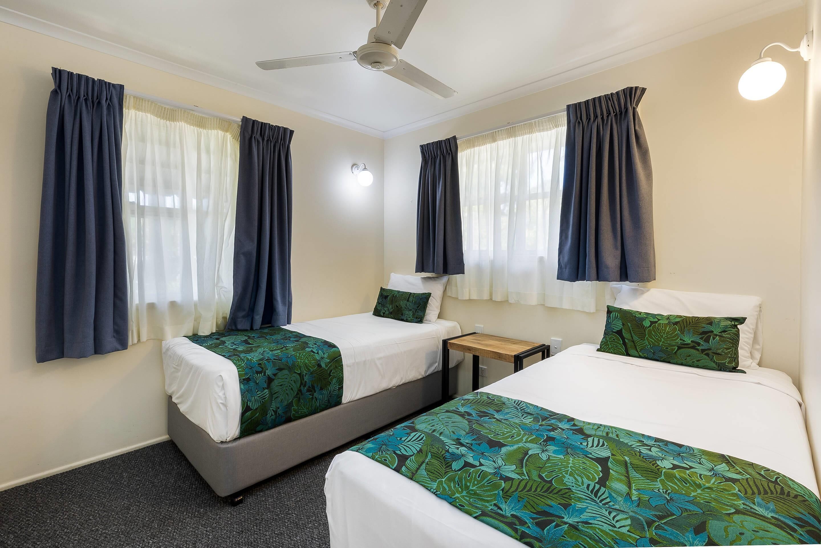 A hotel room with two beds, a ceiling fan, and curtains on the windows.