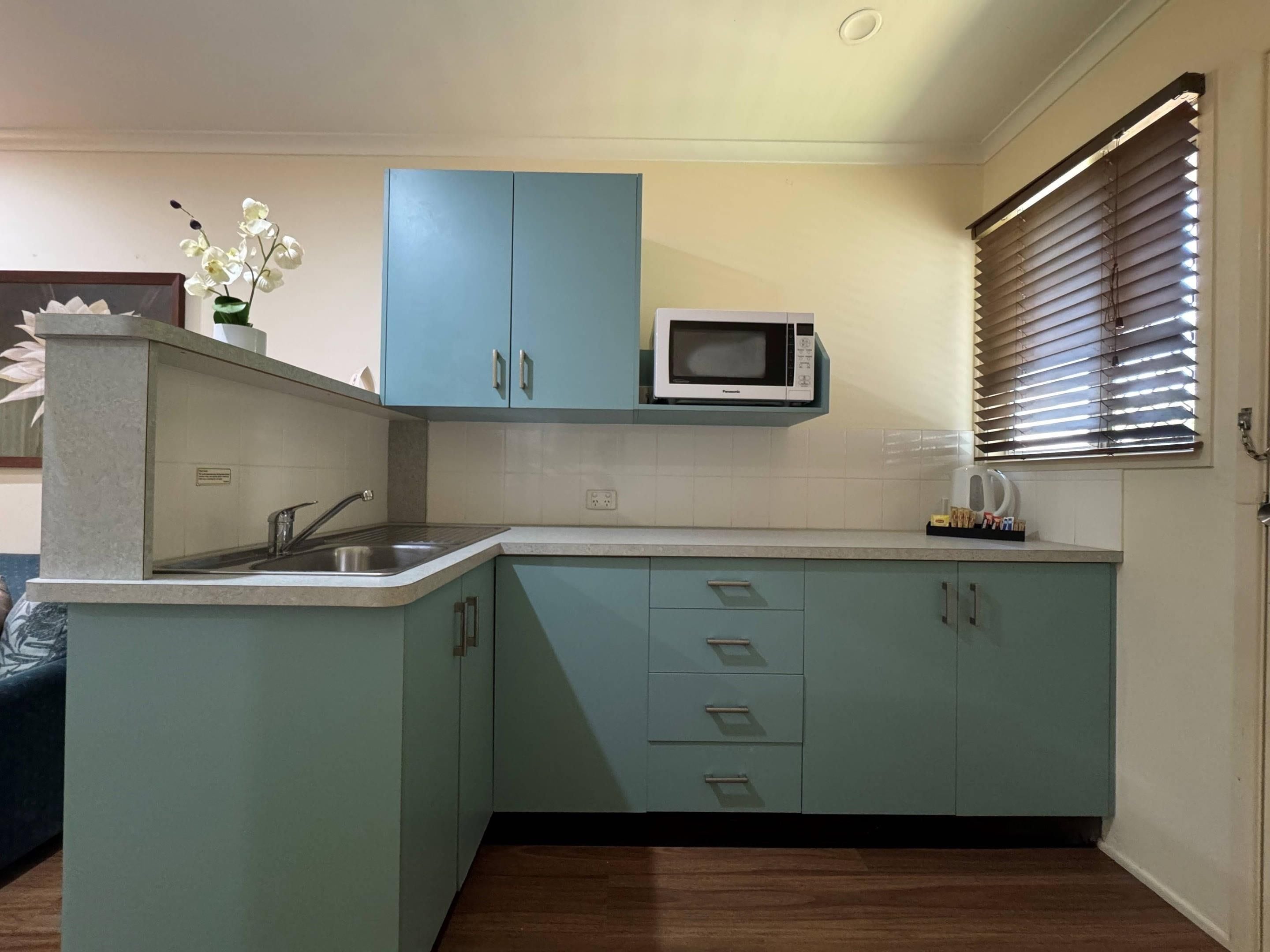A kitchen with teal cabinets, a microwave, a sink, and a window with blinds.