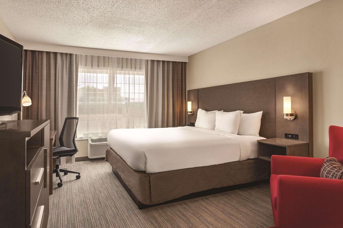 A hotel room with a large bed, a desk, a chair, a TV, and a window with curtains.