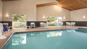 An indoor swimming pool with a wooden ceiling, white lounge chairs, and tables arranged around the pool. - Country Inn & Suites by Radisson, Buffalo, MN (Buffalo)