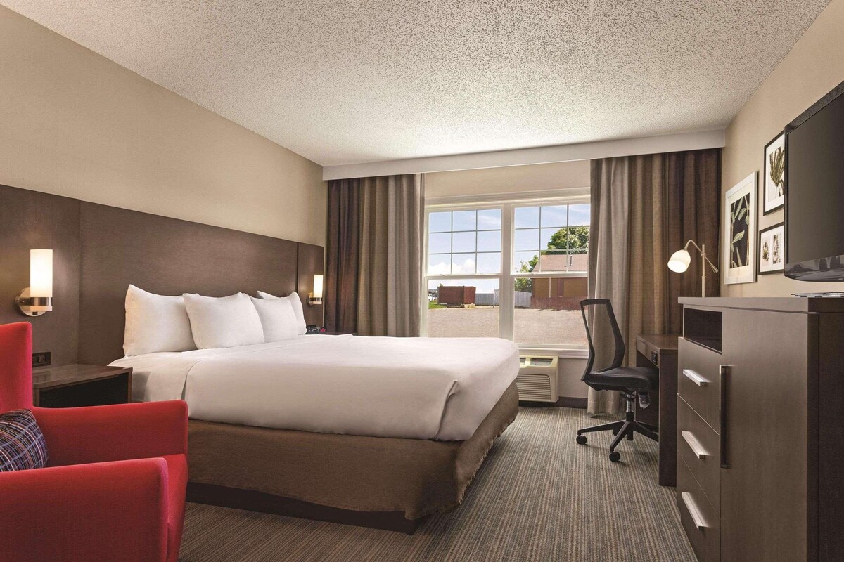 A hotel room with a bed, a desk, a chair, a TV, and a window with curtains.