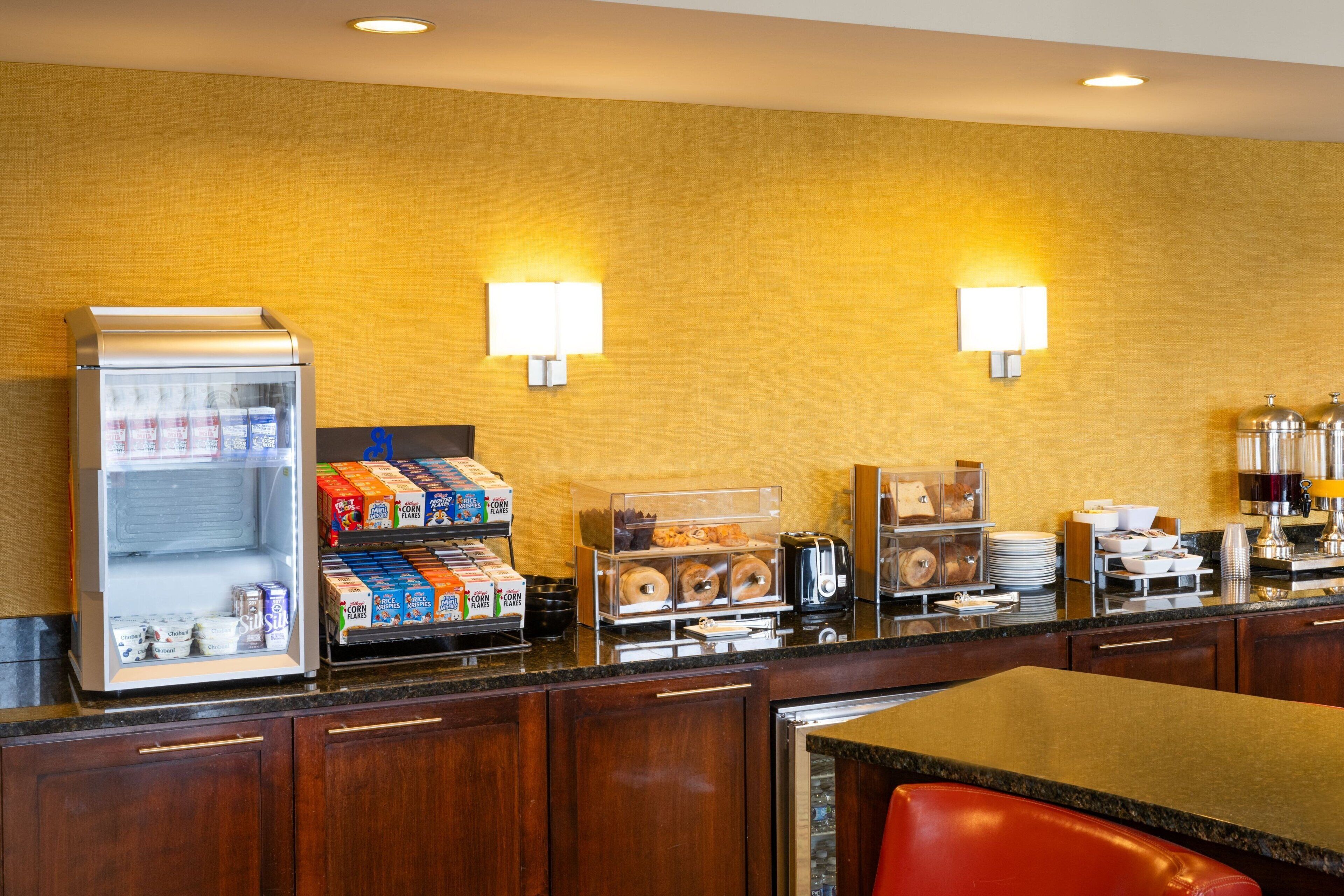 Uma área de pequeno-almoço de hotel com uma máquina de café automática, cereais e pastelaria.