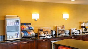 Uma área de pequeno-almoço de hotel com uma máquina de café automática, cereais e pastelaria.