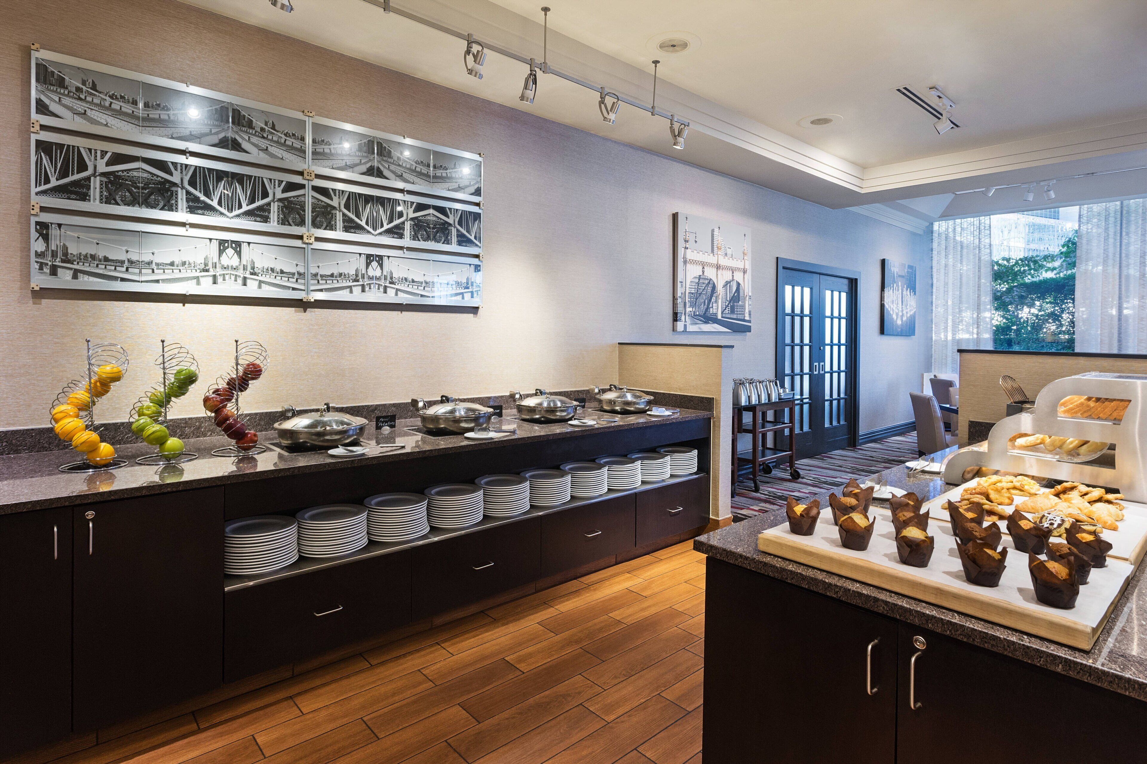 A modern hotel kitchen with a buffet setup, including a variety of dishes and a fruit display.