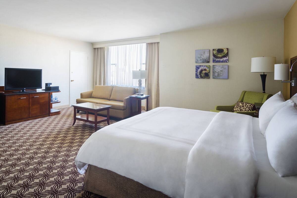 A hotel room with a large bed, a sofa, a television, and a desk.