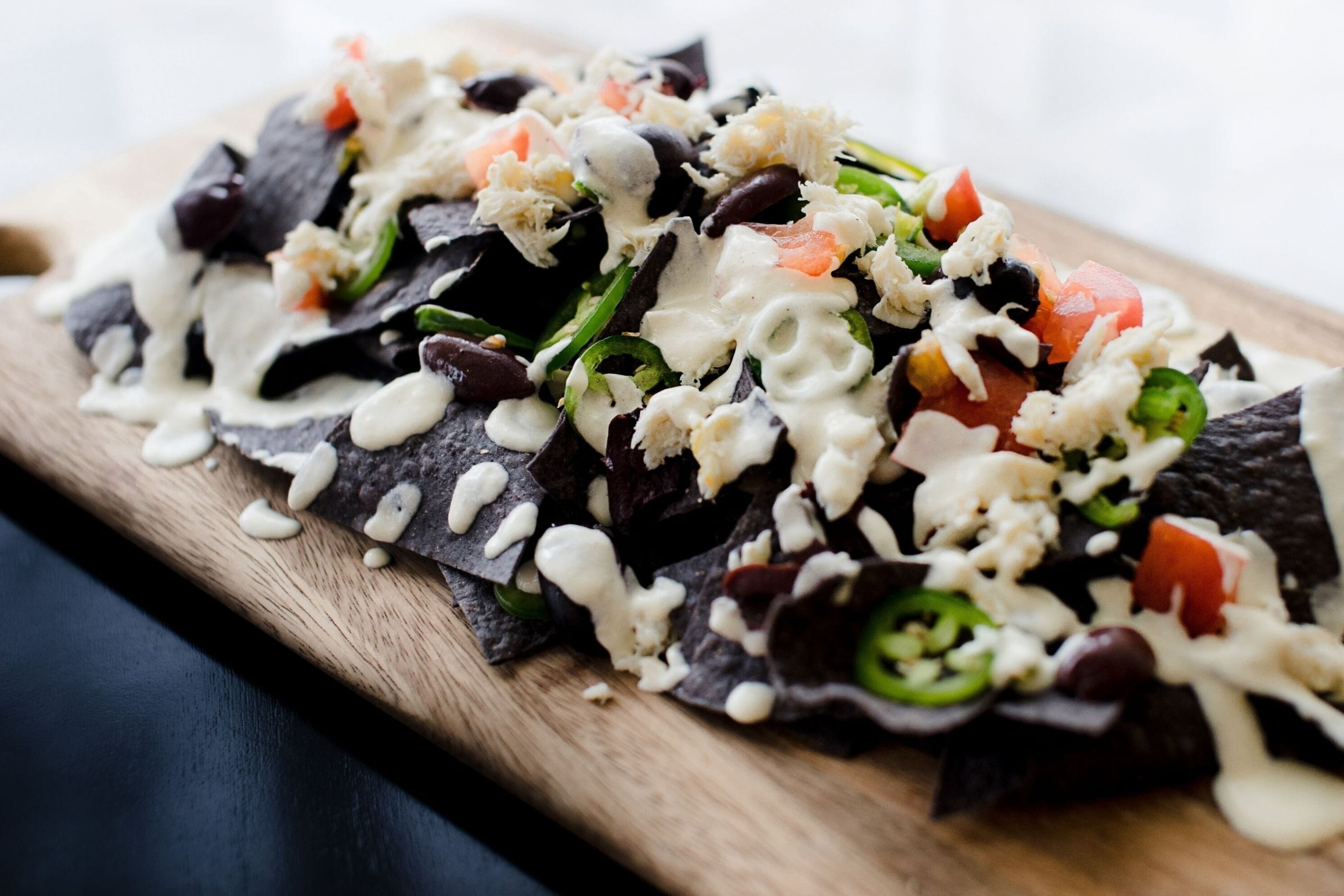 Nachos belegd met zwarte bonen, kaas en groenten op een houten plank.