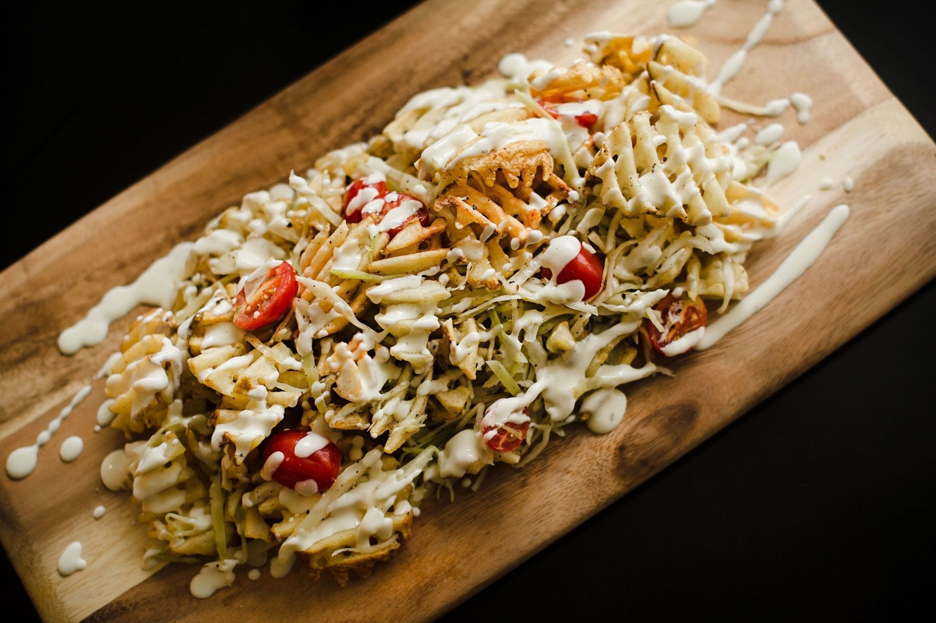 A wooden serving board with a dish of nachos topped with cheese, tomatoes, and a creamy sauce.