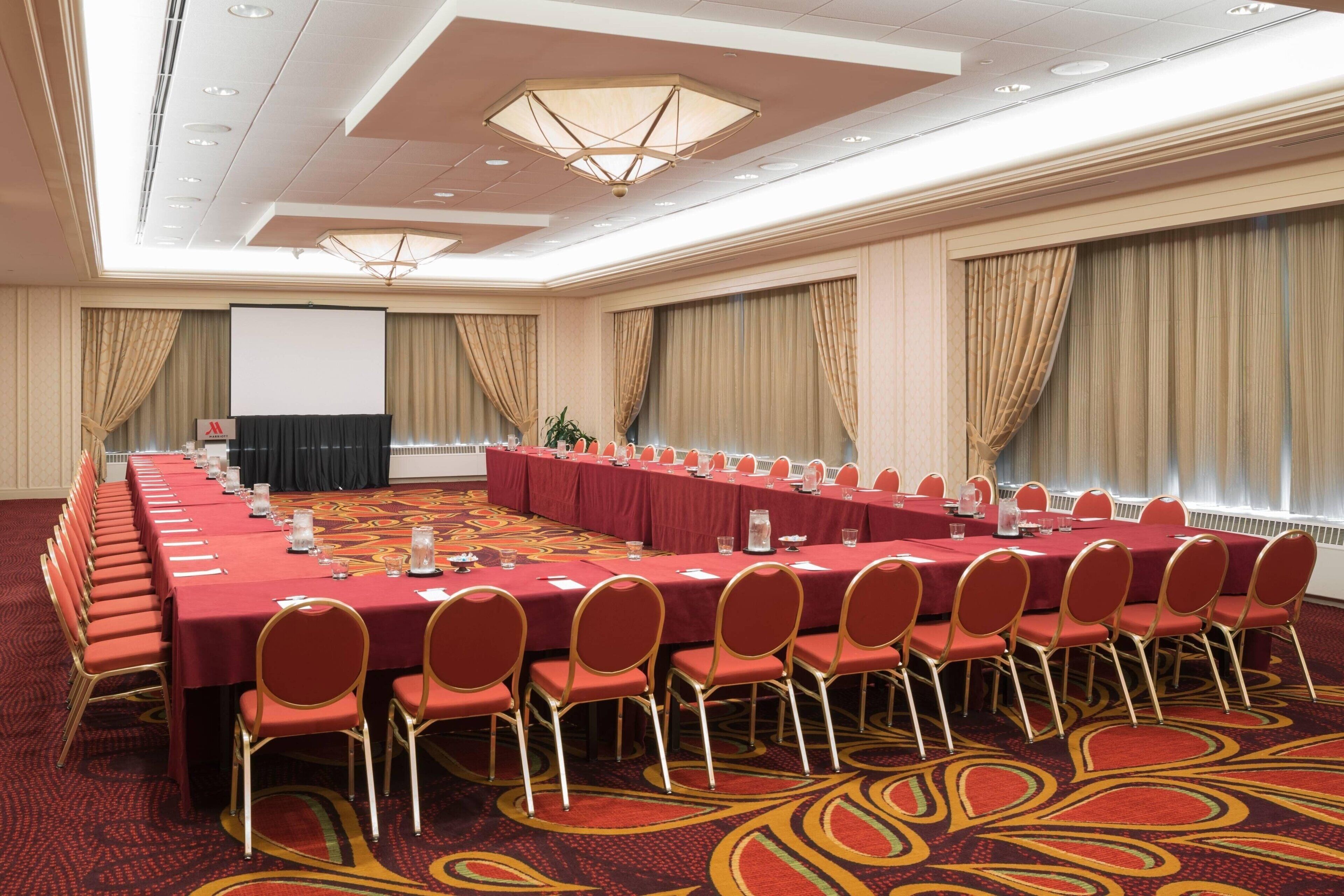 A conference room with a long table, red chairs, and a projector screen.