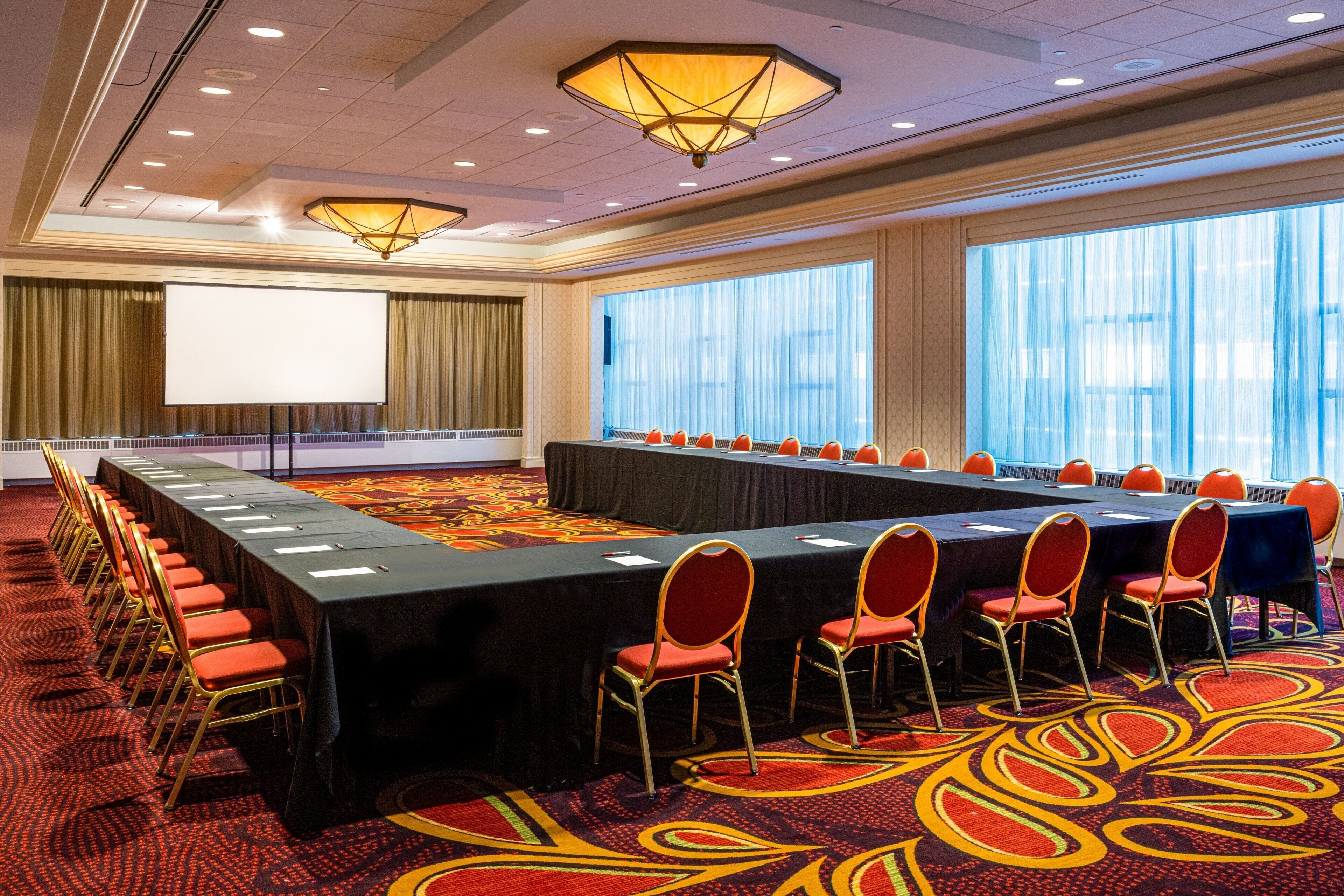 A conference room with a long table, red chairs, and a projector screen.