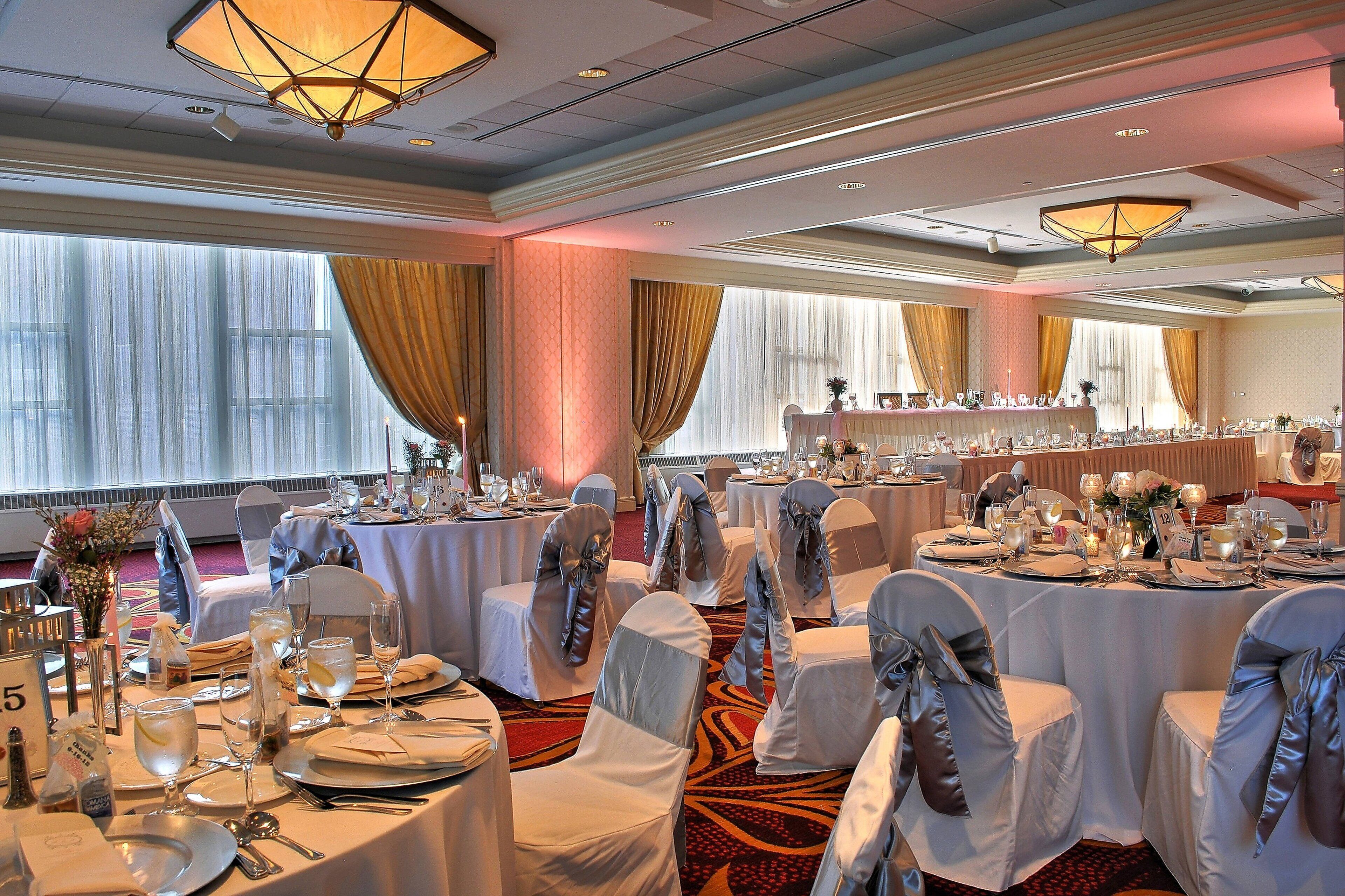 Une salle de banquet avec des tables rondes dressées pour un événement formel, agrémentée de nappes blanches, de couverts en argent et de verres.