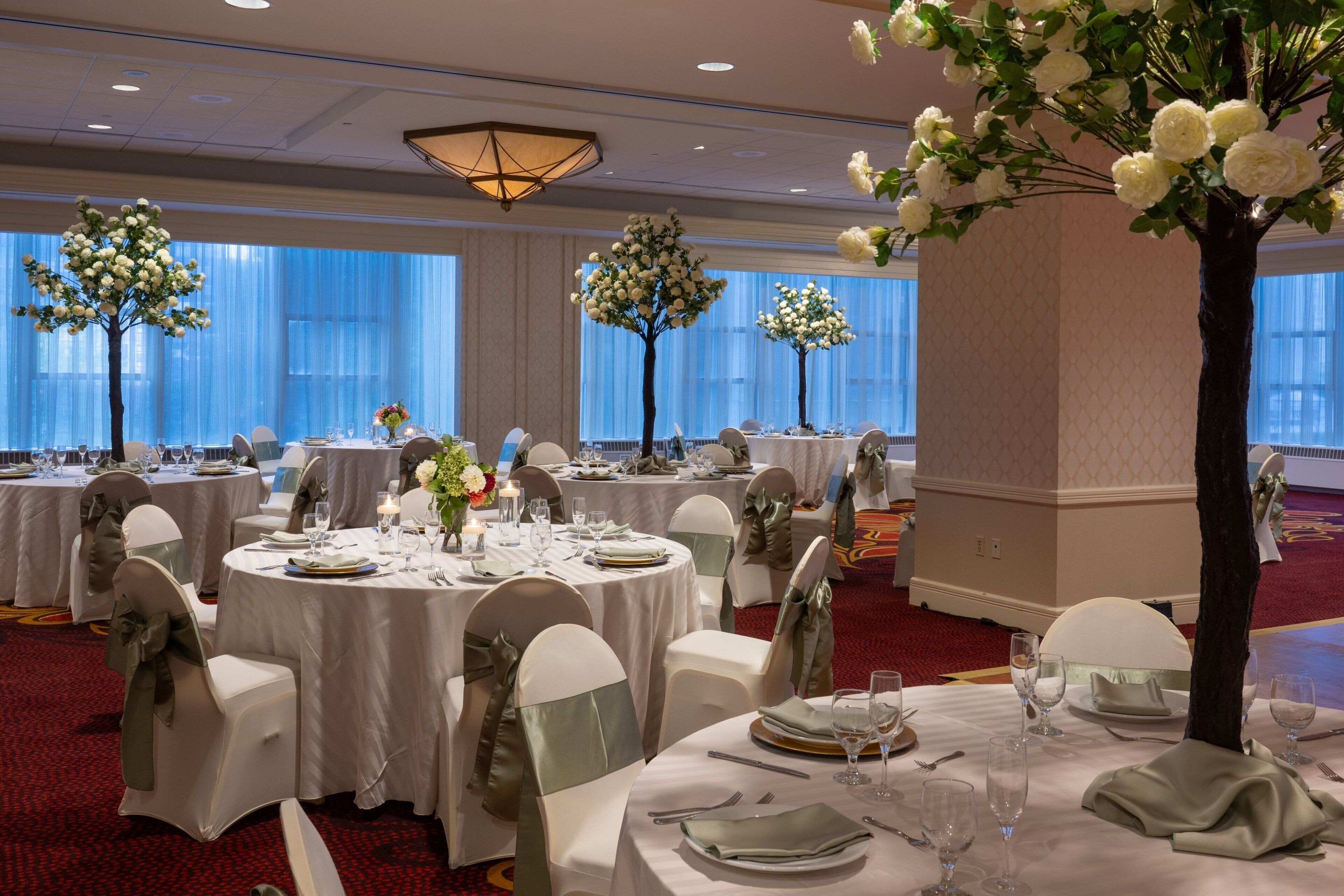 A banquet hall with round tables, white tablecloths, and floral centerpieces.
