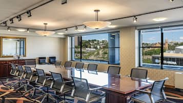 A conference room with a large table, chairs, and a view of a cityscape through large windows.