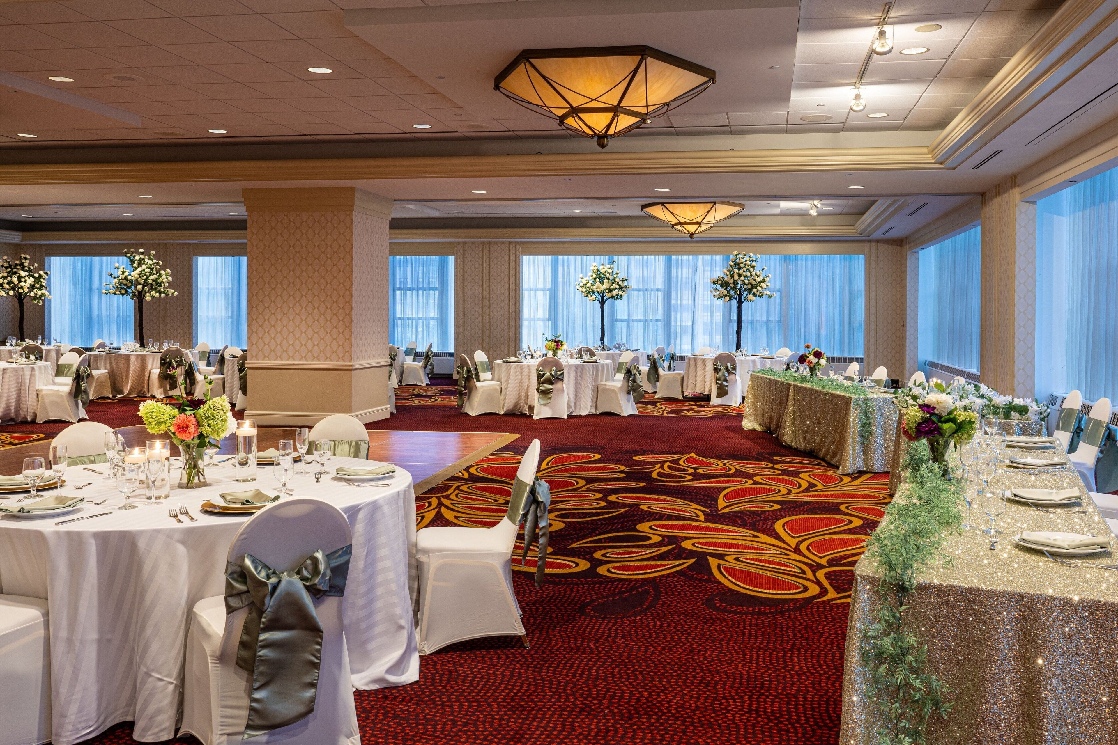A banquet hall with round tables set for a formal event, featuring white tablecloths, chairs, and floral centerpieces.