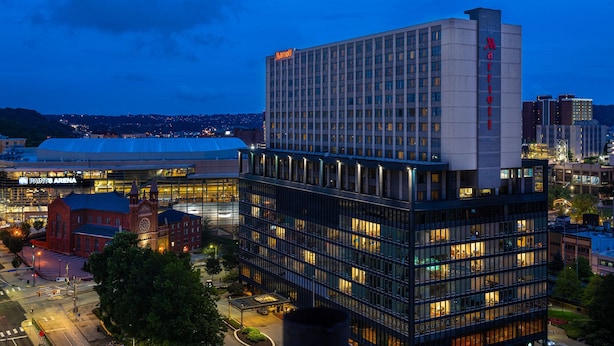 Ett Marriott-hotell med en modern fasad av glas, omgivet av andra byggnader och en historisk byggnad i bakgrunden.