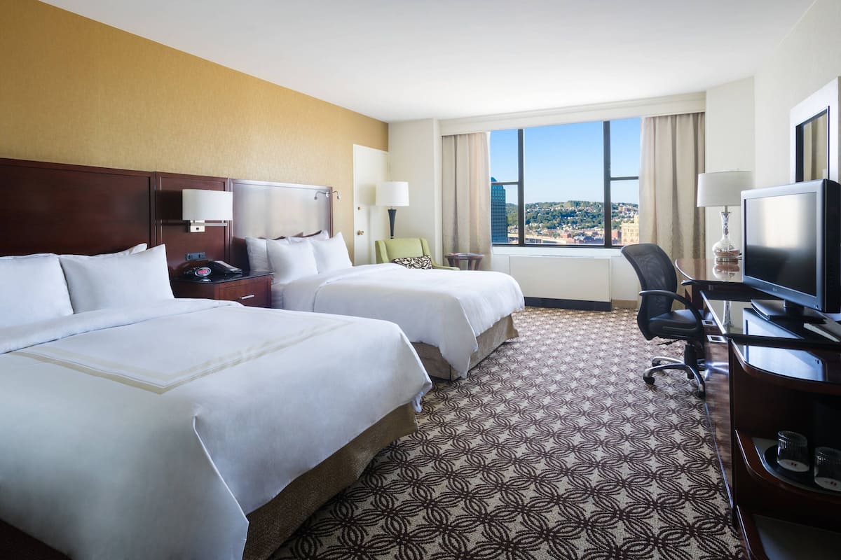 A hotel room with two beds, a desk with a computer, a TV, and a view of the city.