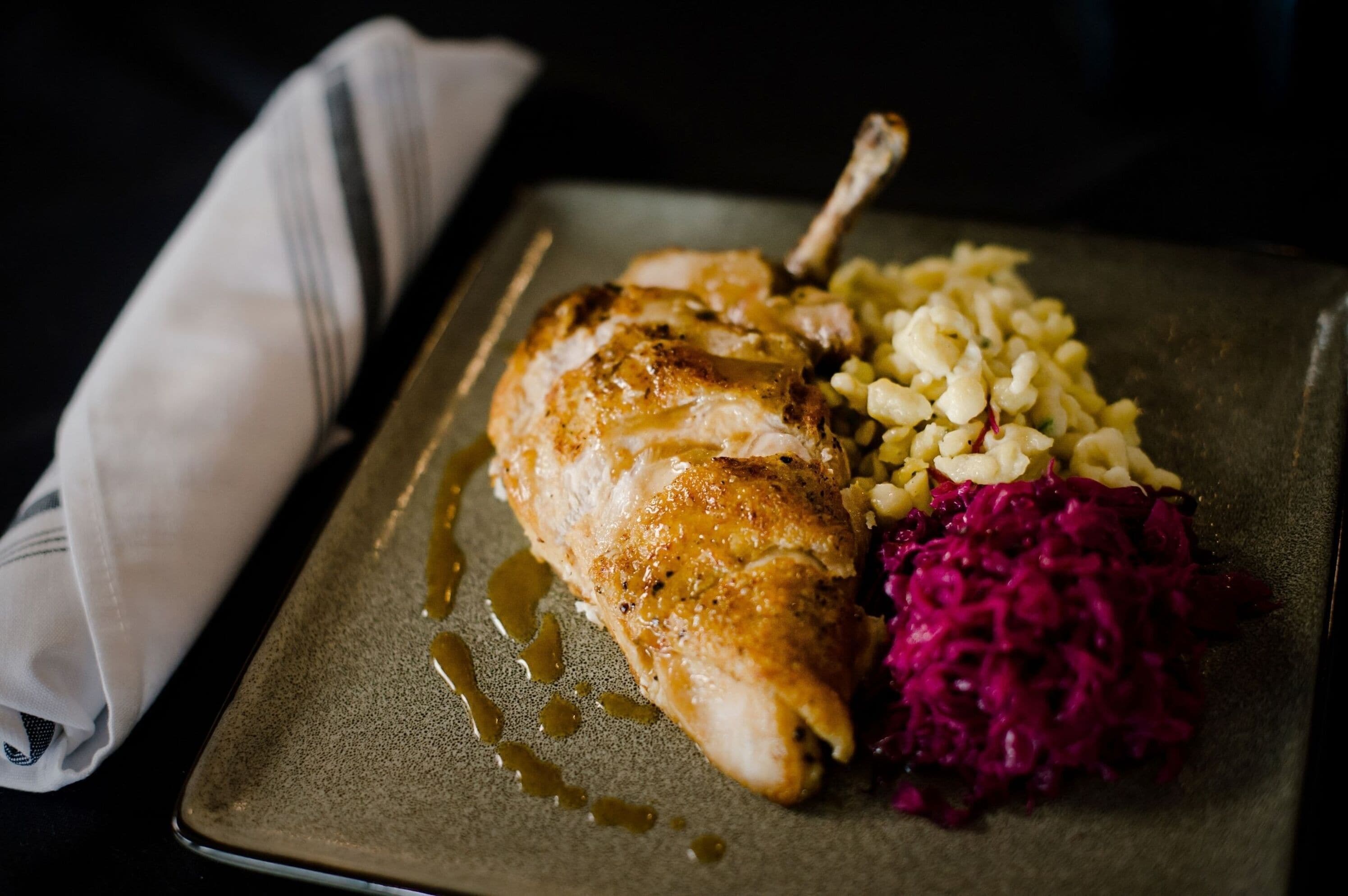 A plate with a piece of meat, possibly chicken, accompanied by a side of what appears to be sauerkraut and a grain dish, possibly barley.