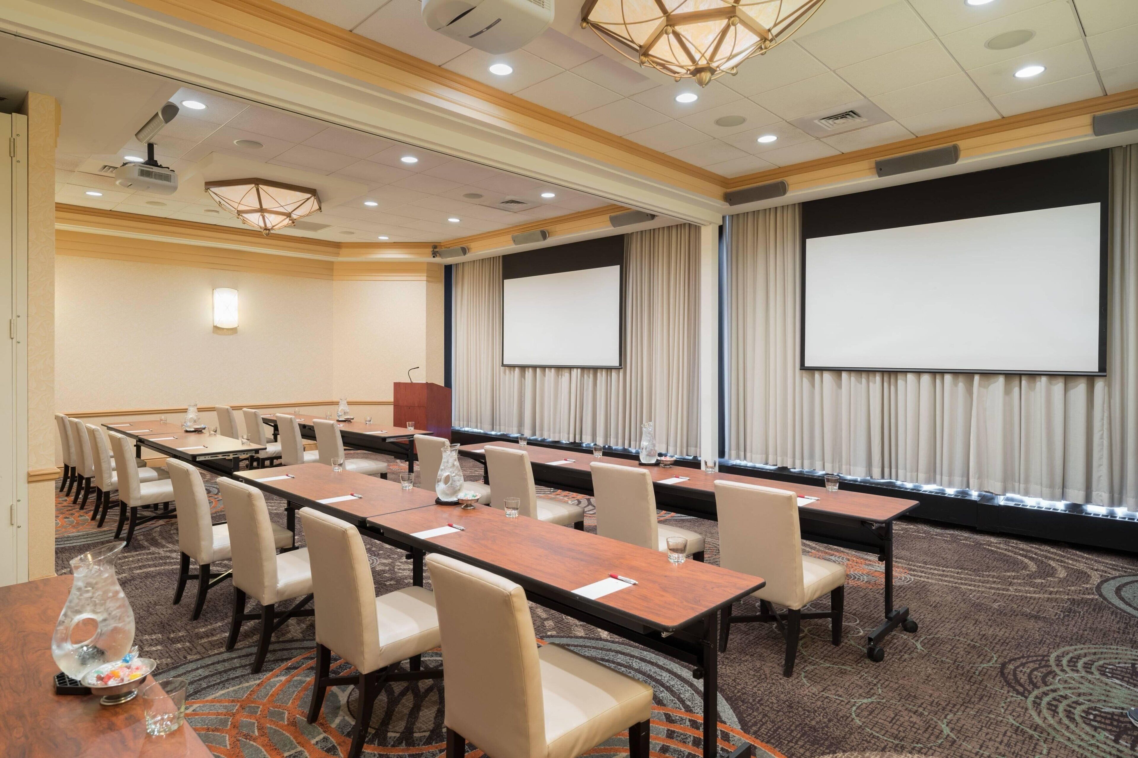 A conference room with multiple tables and chairs, a projector screen, and a podium.