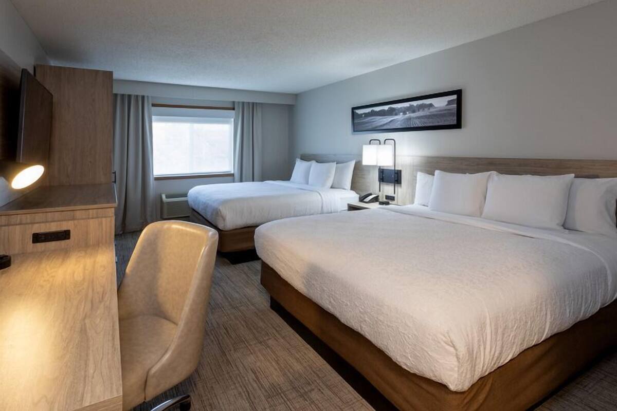 Une chambre d’hôtel avec deux lits, un bureau, une chaise, une lampe de bureau, un téléphone et une fenêtre avec des rideaux.