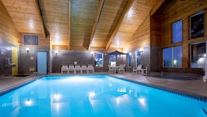 En inomhuspool med väggar och tak av trä, omgiven av solstolar och ett litet bord.