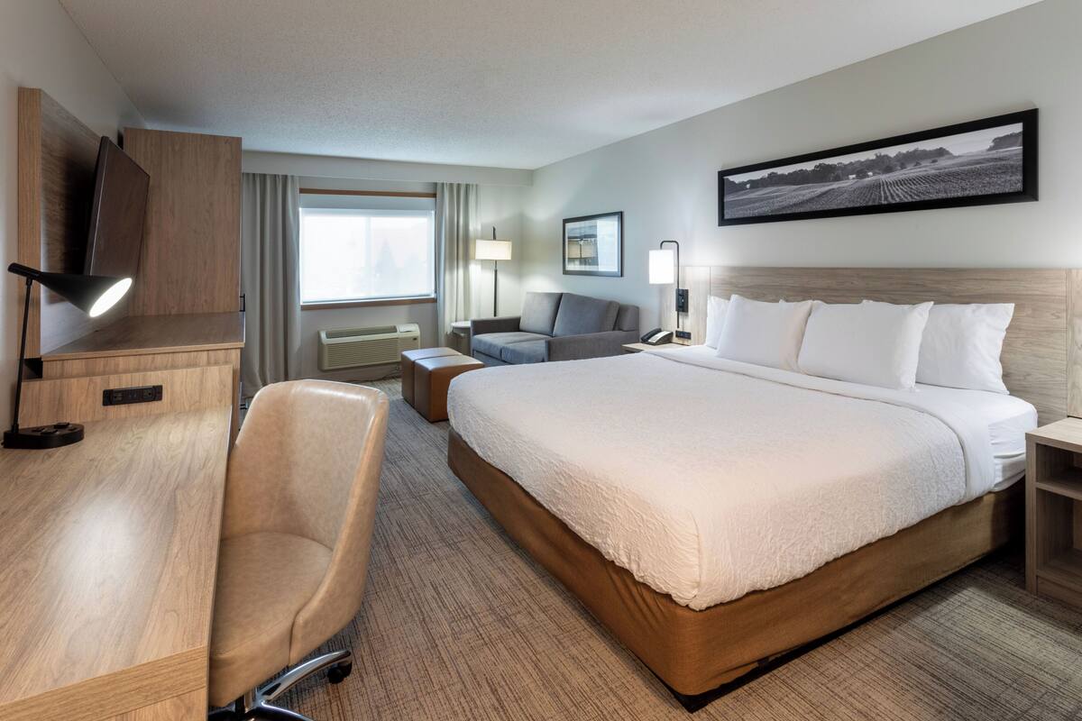 Une chambre d’hôtel avec un grand lit, un bureau avec une chaise, une télévision et une fenêtre avec des rideaux.