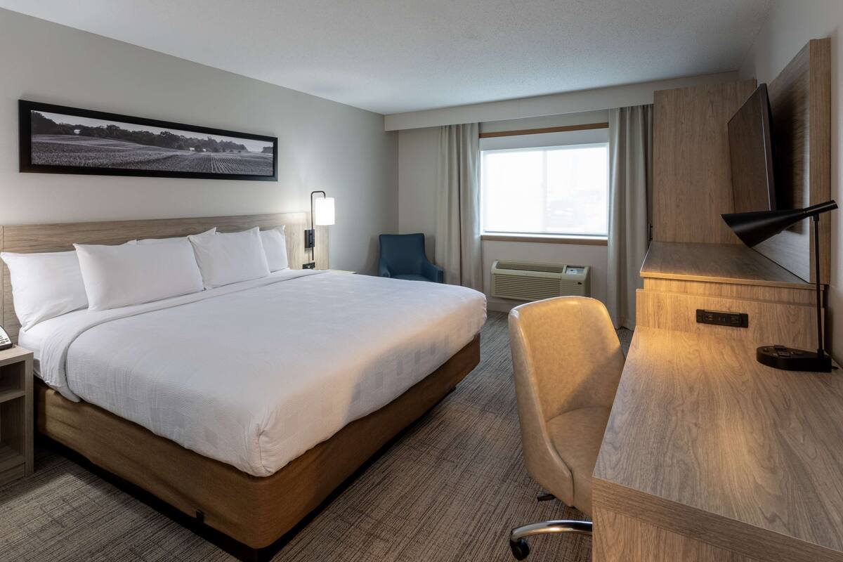 Une chambre d’hôtel avec un grand lit, un bureau, une chaise, une télévision et une fenêtre avec des rideaux.