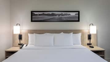 A hotel room with a large bed, two bedside tables, a mounted picture, and wall-mounted lamps.