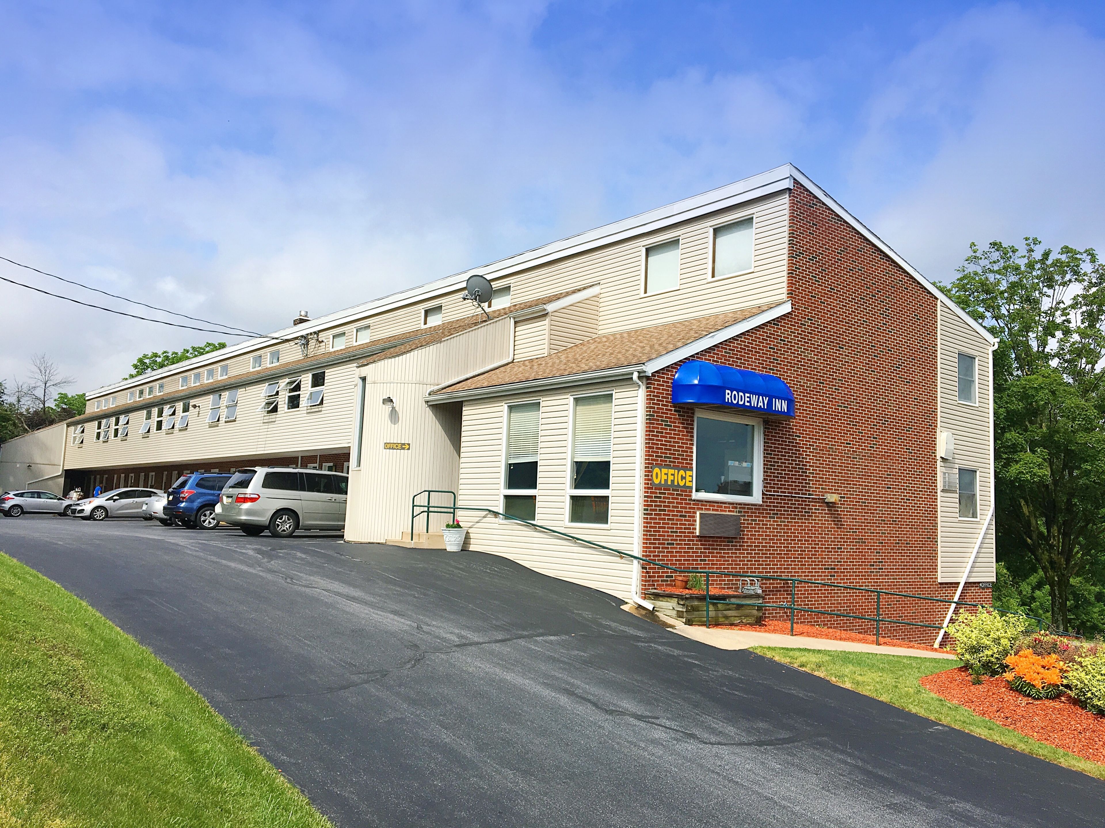 A motel with a blue awning labeled "RODEWAY INN" and a sign indicating an office.