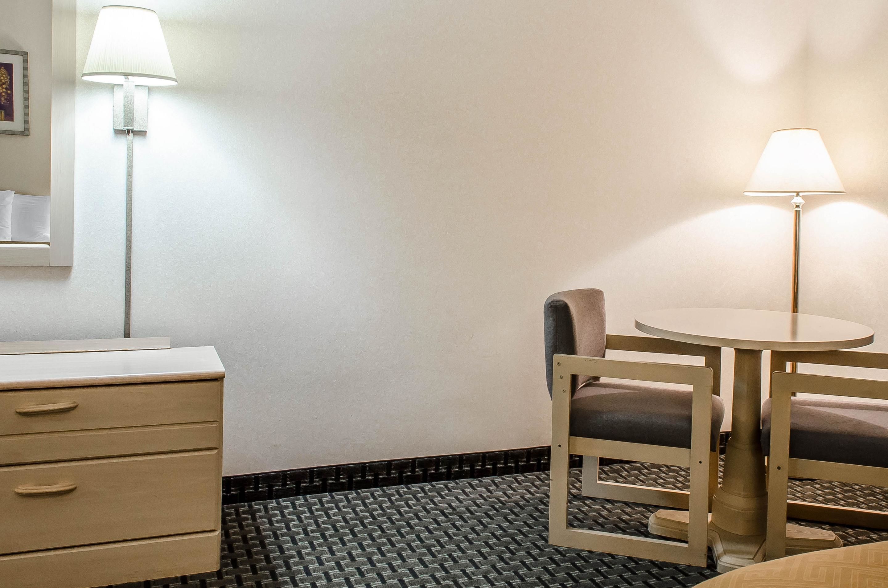 Une chambre d’hôtel avec un lit, une table de chevet, une lampe, une chaise et une petite table ronde.