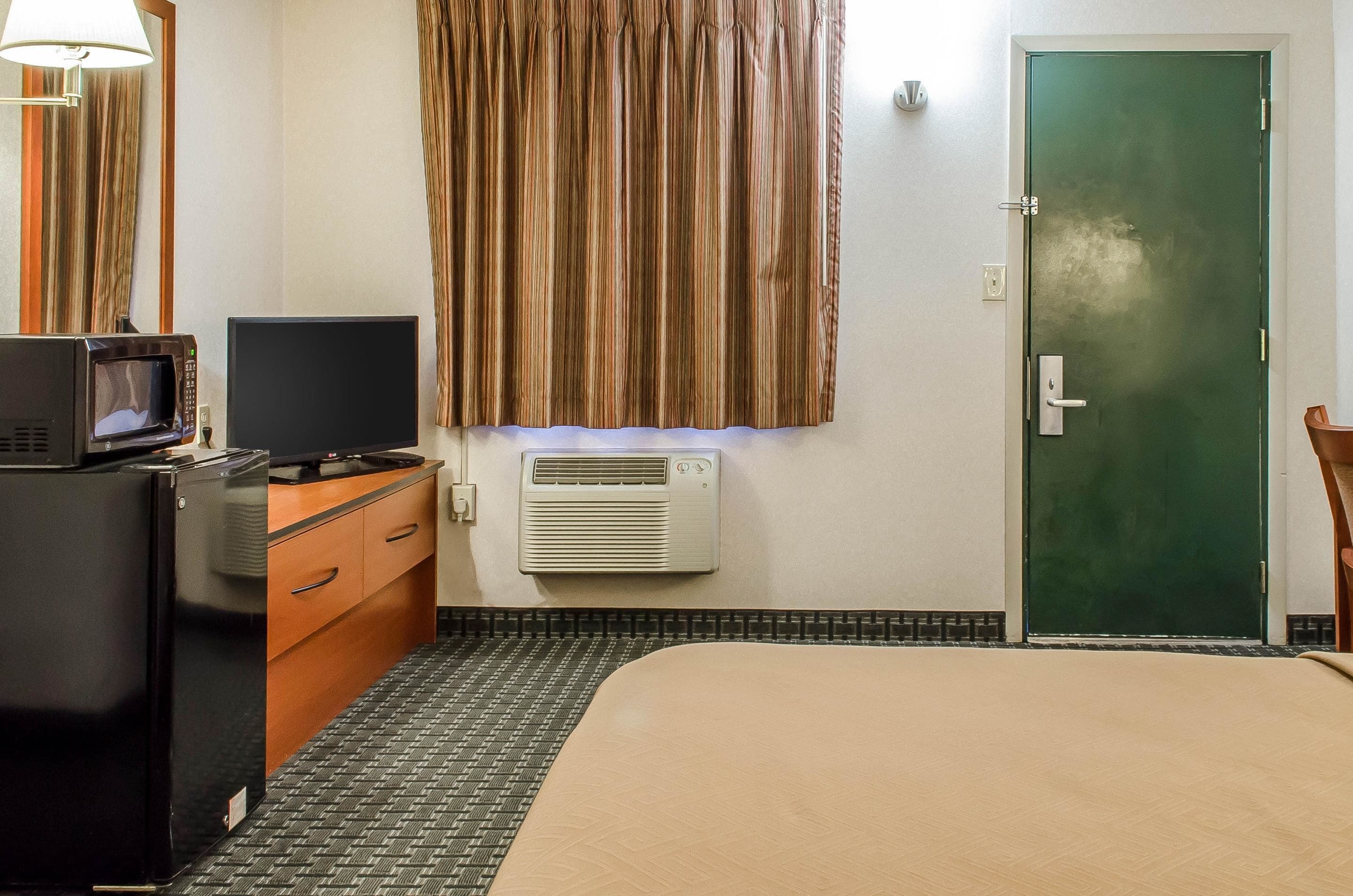 Hotelkamer met een bed, een bureau met een magnetron, een televisie, een kledingkast en een airconditioningsysteem, plus een groene deur.
