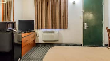 Hotelkamer met een bed, een bureau met een magnetron, een televisie, een kledingkast en een airconditioningsysteem, plus een groene deur.