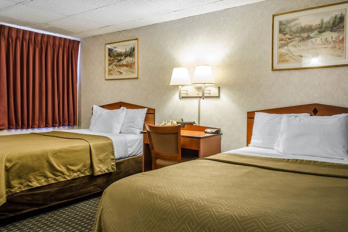 A hotel room with two beds, a desk, a chair, a lamp, and two paintings on the walls.