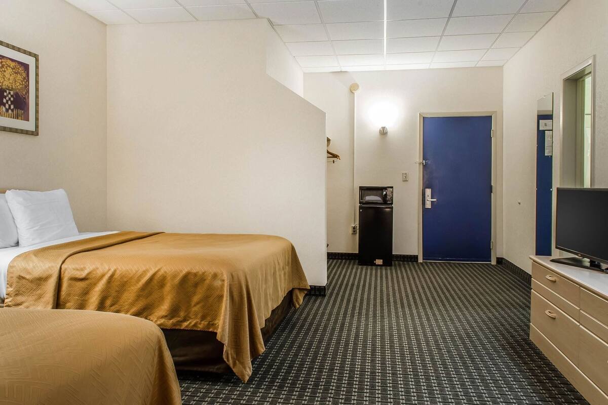 A hotel room with two beds, a television, a desk, and a door.