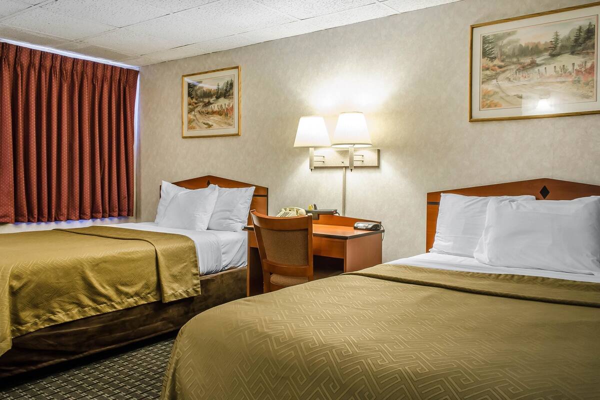 A hotel room with two beds, a desk, a chair, a telephone, and two wall-mounted lamps.