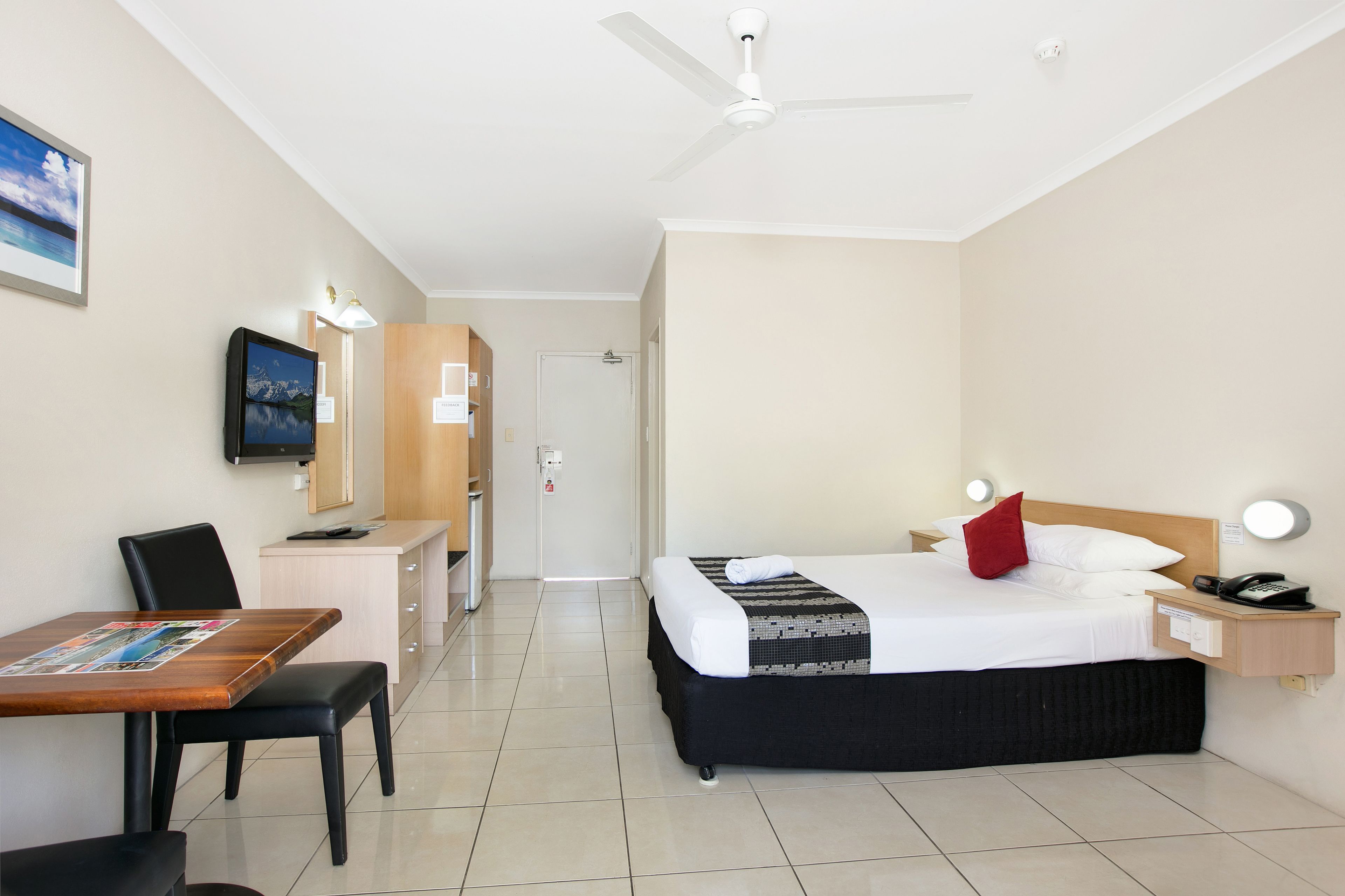 A hotel room with a bed, desk, chair, and a television on the wall.
