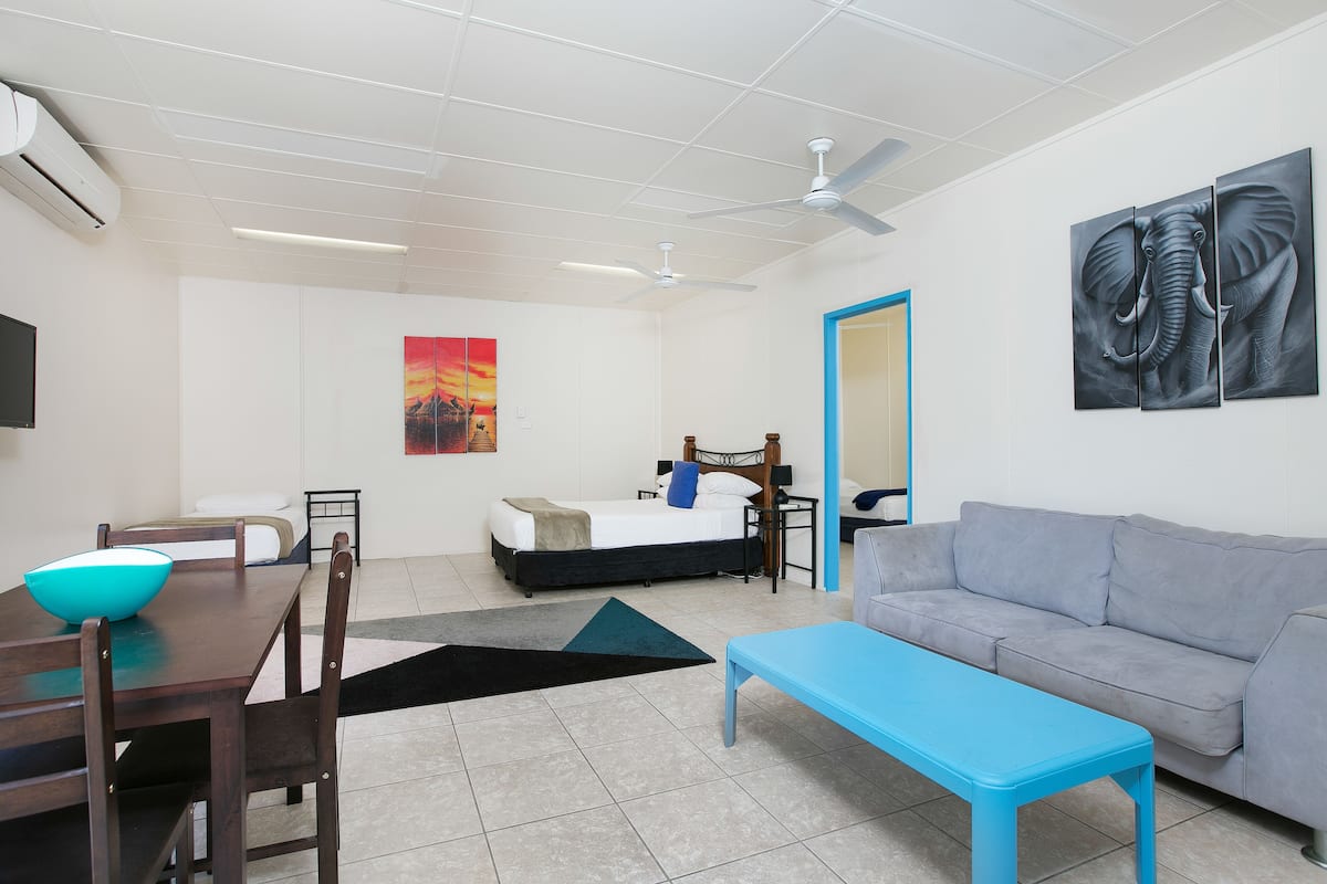 Quarto moderno com cama, sofá, mesa de jantar com cadeiras, um banco azul e um ventilador de teto.
