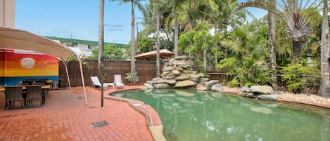A pool area with lounge chairs, a covered seating area, and a stone waterfall feature.