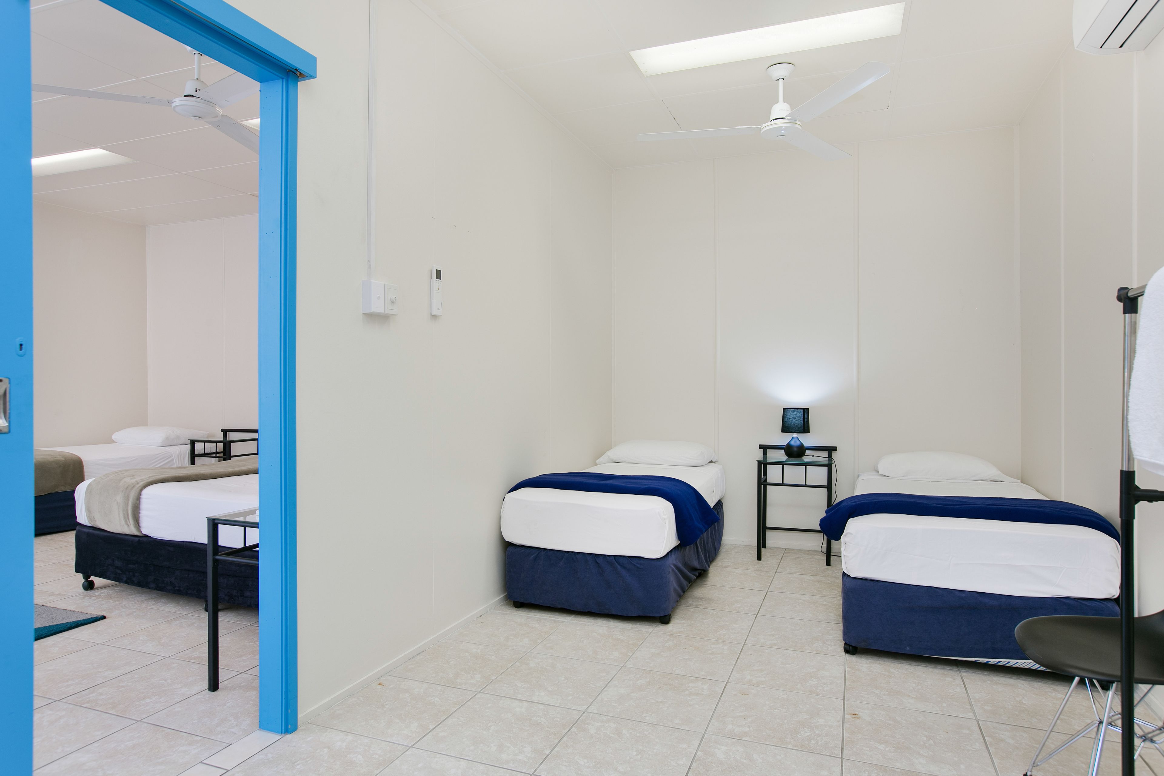 A hotel room with two beds, a ceiling fan, a small table with a lamp, and a chair.