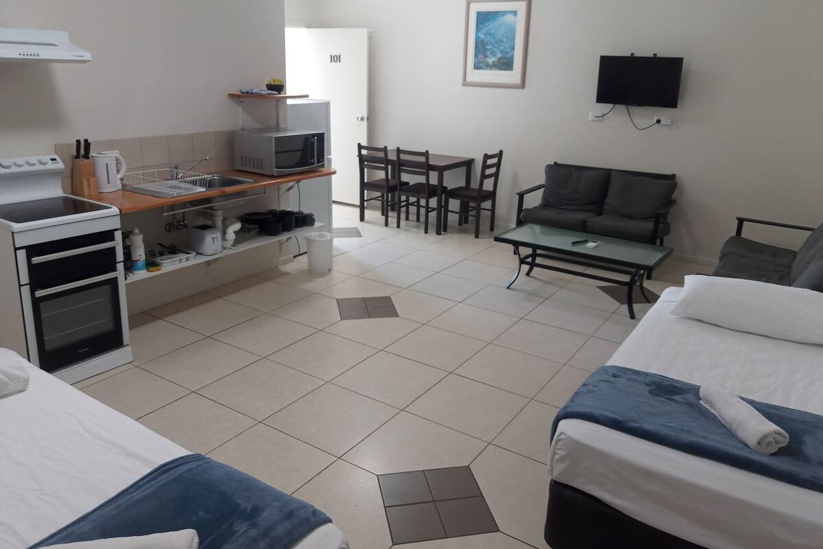 Quarto de hotel com cozinha compacta, área de refeições, televisão e duas camas.