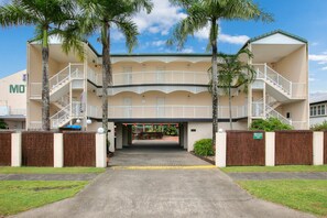 Un hotel de varios pisos con una entrada central, palmeras y cielo despejado.
