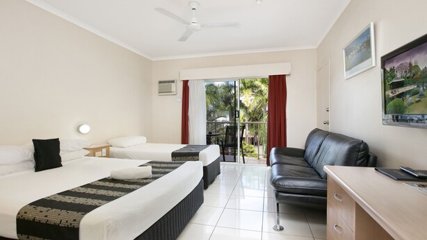 Habitación de hotel con dos camas, un escritorio, una silla, un ventilador de techo y vistas al exterior.