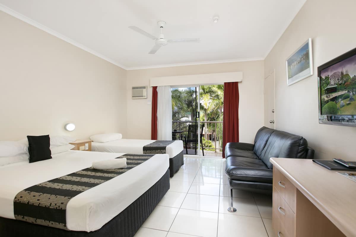 Quarto de hotel com duas camas, uma escrivaninha, uma cadeira, ventoinha no teto e vista para o exterior.