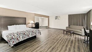 A hotel room with a bed, a sofa, a desk, a chair, a lamp, and a bathroom visible through an open door. - Red Roof Inn & Suites Duncan (Duncan)