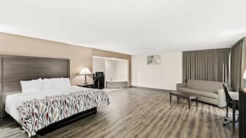 Een hotelkamer met een bed, een bank, een bureau, een stoel, een lamp en een badkamer zichtbaar door een open deur.
