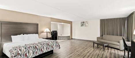A hotel room with a bed, a sofa, a desk, a chair, a lamp, and a bathroom visible through an open door.