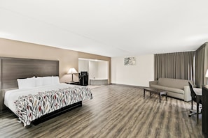 A hotel room with a bed, a sofa, a desk, a chair, a lamp, and a bathroom visible through an open door. - Red Roof Inn & Suites Duncan (Duncan)