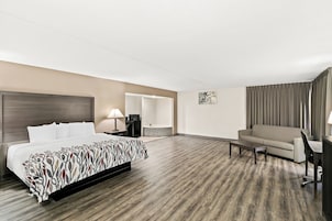 Habitación de hotel con cama, sofá, escritorio, silla, lámpara y baño visible a través de una puerta abierta.